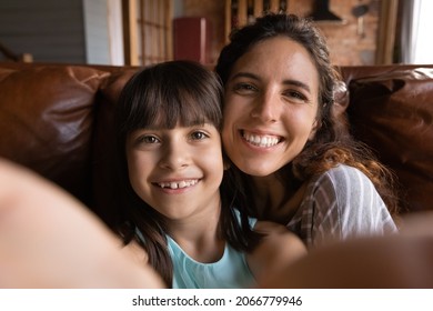 Happy Young Latin Mum And Cute Daughter Girl Taking Selfie With Face Touch, Holding Smartphone, Gadget, Looking At Camera, Smiling. Cheerful Mother And Kid Having Fun At Home. Close Up Portrait