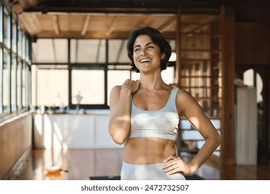 Happy young Latin woman yoga coach laughing standing in yoga gym studio. Smiling fit Hispanic lady in her 30s advertising yoga classes. Sporty healthy female trainer wearing sportswear looking away. - Powered by Shutterstock