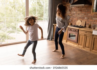 Happy Young Latino Mother And Excited Little 8s Daughter Dance Together In Modern Renovated Kitchen Together. Overjoyed Hispanic Mom Or Nanny Have Fun With Small Teen Girl Child At Home. Rent Concept.