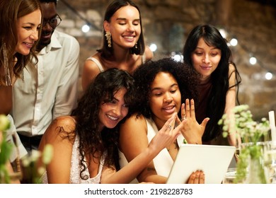 Happy Young Lesbian Newlyweds In Wedding Attire Boasting With Their Rings While Communicating In Video Chat Among Guests