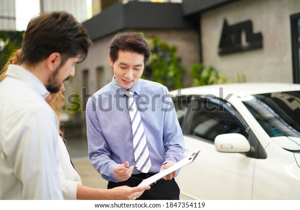 Happy young lovely couple in a\
car salon. taking car to the repair shop to be fixed  together in\
dealership. salesman explaining all the car features to the\
couple