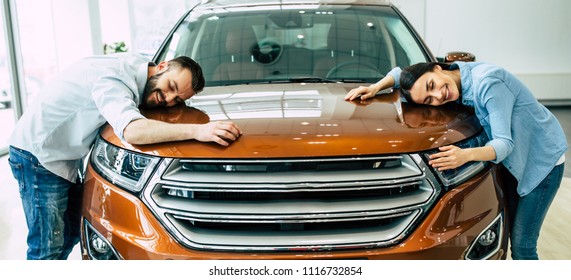 Happy Young Lovely Couple In Casual Wear Buying First New Family Car Together In Dealership.