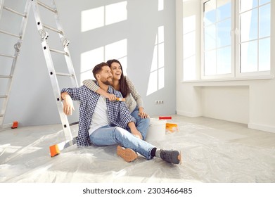 Happy young loving couple planning home repair while sitting on floor in living room. Cheerful wife hugging her husband in freshly painted room. Home repair and decoration concept - Powered by Shutterstock