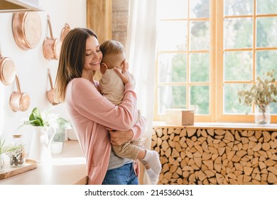 Happy Young Loving Mother Holding Hugging Embracing Little Small Kid Child Son Toddler, Nurturing, Singing Lullaby At Home Kitchen. Motherhood Concept