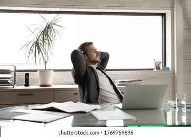 Happy young male boss relax lean back in chair in office look in distance dreaming or thinking, calm Caucasian businessman rest at workplace, breathe fresh air, take break, stress free concept