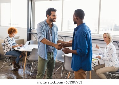 Happy Young Male Business People Shaking Hands At Creative Office