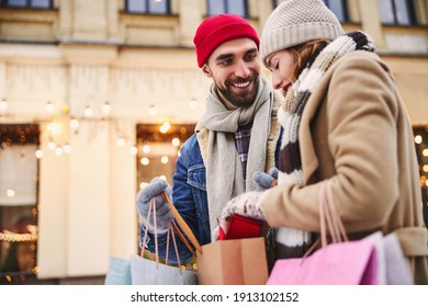 Happy young male is buying presents for beloved woman while they are walking in snowy street