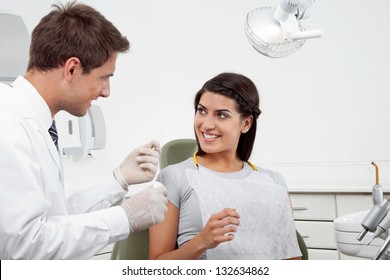 Happy Young Male Dentist Holding Thread While Patient Looking At Him In Clinic