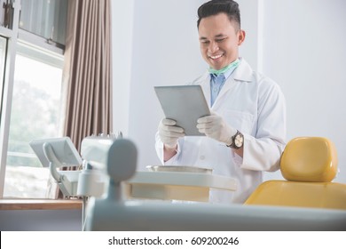 Happy Young Male Dentist With Tablet Over Medical Office Clinic