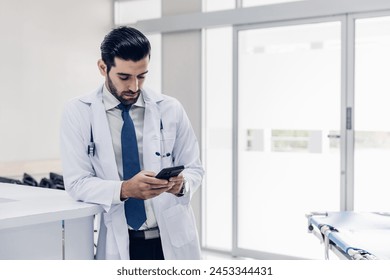 Happy young male  doctor in  white coat Standing using cellphone applications in clinic office.  Man with healthcare, medical and wellness app on mobile technology or search internet - Powered by Shutterstock