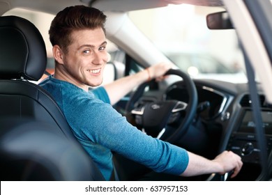 Happy young male driver behind the wheel. The guy in the car. Lifestyle scene in the car dealership