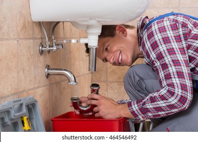 Happy Young Male Plumber Installing Sink Pipe In Bathroom