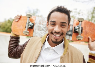 Happy young male skateboarder being delightful after spending morning Saturday outdoors, rides skateboard, smiles happily, improved skills of riding. Sporty teenage skater with joyful expression