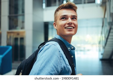 Happy young male student looking back and smiling in college. University student with his bag in campus.