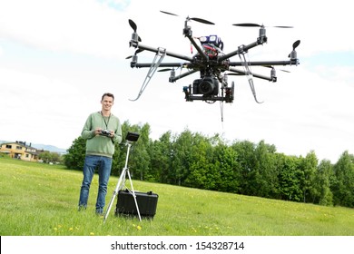 Happy young male technician flying UAV octocopter with remote control in park