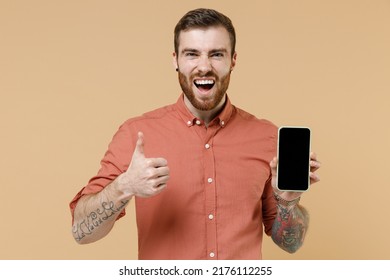 Happy young man 20s he wear orange shirt hold in hand use mobile cell phone with blank black screen workspace area isolated on plain pastel light beige background studio portrait. Tattoo translate fun