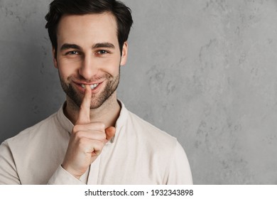 Happy young man asking for silence gesturing with his finger isolated over gray background - Shutterstock ID 1932343898