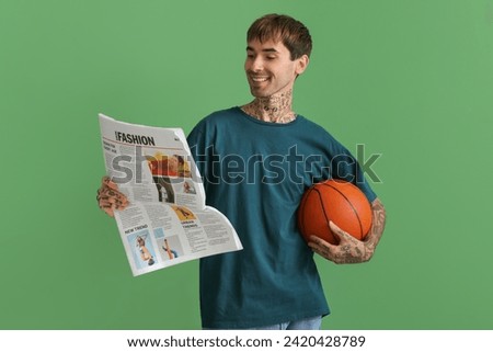 Happy young man with ball for basketball and newspaper on green background