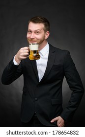 Happy Young Man In A Black Suit Holding A Beer Mug Over A Dark Background