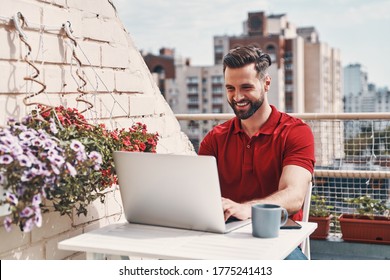 Happy young man in casual clothing using laptop while sitting on the rooftop patio  - Powered by Shutterstock