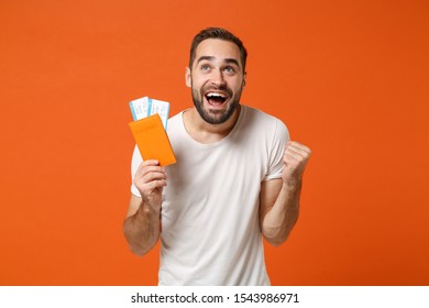 Happy young man in casual white t-shirt posing isolated on orange background studio portrait. People lifestyle concept. Mock up copy space. Holding passport boarding pass ticket, doing winner gesture - Shutterstock ID 1543986971