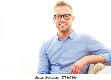 Happy Young Man. Close Up Portrait Or Head Shot Of Handsome Young Man In Casual Blue Shirt And Dioptrical Glasses Sitting In Comfortable Pose Isolated On White Background