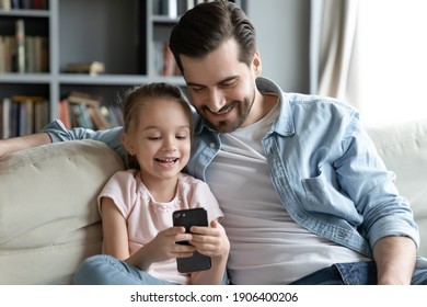 Happy young man cuddling little 6s daughter, playing together on smartphone. Smiling small preschool girl enjoying using mobile applications or watching funny video sitting with caring daddy on sofa. - Powered by Shutterstock