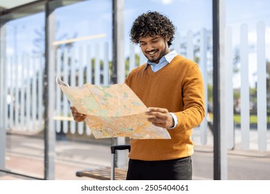 Happy young man with curly hair exploring city using map, standing at bus stop with suitcase. Captures travel, adventure, and navigation on bright sunny day. - Powered by Shutterstock