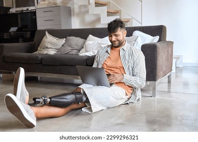 Happy young man with disability leg prosthesis sitting on floor at home using laptop computer working or elearning, browsing web, searching online. People with amputation disabilities everyday life. - Powered by Shutterstock