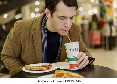 Happy Young Man Eating Pizza At The Food Court In A Mall