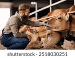 Happy young man farm worker takes care of cows in barn. Concept cattle livestock farming, industry agriculture.