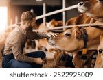 Happy young man farm worker takes care of cows in barn. Concept cattle livestock farming, industry agriculture.