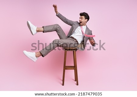 Happy young man in full suit having fun while sitting on the chair against pink background