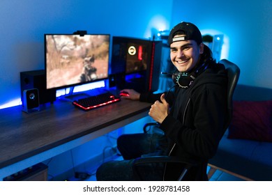 Happy Young Man Giving A Thumbs Up While Sitting In Front Of A Gaming PC. Male Gamer Playing An Online Video Game In His Bedroom Desk