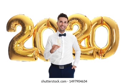 Happy Young Man With Glass Of Champagne Near Golden 2020 Balloons On White Background. New Year Celebration