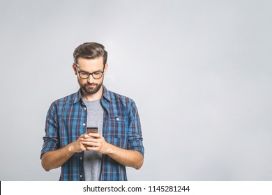 Fröhlicher junger Mann mit einer Brille, die auf grauem Hintergrund SMS schreibt