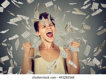 Happy young man going crazy screaming super excited. Ecstatic guy celebrates success under money rain falling down dollar bills banknotes isolated gray background. Financial freedom concept