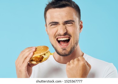 happy young man with a hamburger in his hand laughs at the camera on a blue background and narrowed his eyes