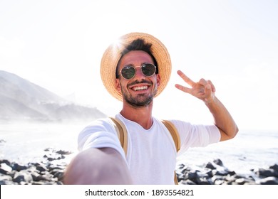 Happy young man with hat and backpack taking a selfie portrait hiking on mountains - Pov view of a smiling guy using smart phone mobile  - Shutterstock ID 1893554821
