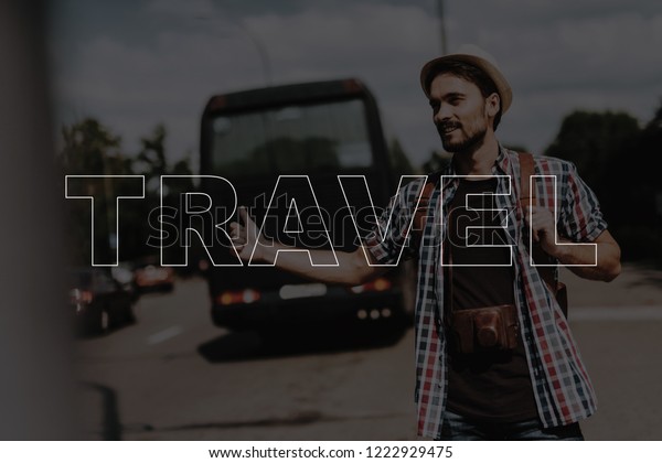 Happy Young Man is Hitchhiking. Concept of Travel\
and Adventures. Hipster Hiker on Vacation. Happy Tourist in Summer\
Day. Carefree Guy on Roadside. Smiling Man with Camera.\
Photographer Catches Car.