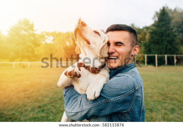 Happy young man holding dog Labrador in hands at sunset\
outdoors 