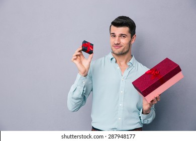 Happy Young Man Holding Small And Big Gift Box Over Gray Background