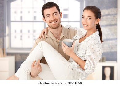 Fröhlicher junger Mann, der eine Frau in den Armen hält, eine Frau, die Tee trinkt, lächelt?