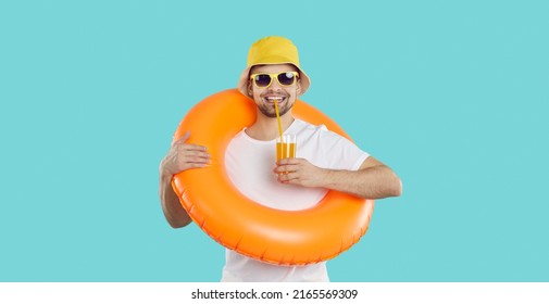 Happy young man with inflatable swimming circle and with glass of juice enjoys summer vacation. Cheerful funny guy in summer clothes drinks juice on light blue background. Summer relaxation concept. - Shutterstock ID 2165569309