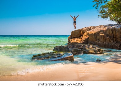 The happy young man jumping off cliff into the ocean. Summer fun, lifestyle, extreme sport. - Powered by Shutterstock
