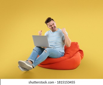 Happy Young Man With Laptop On Bean Bag Chair, Yellow Background