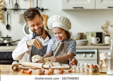 Joven feliz con su pequeña hija en un sombrero de chef que amasan la masa mientras preparan pasteles y disfrutan juntos en la cocina de casa
