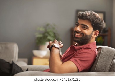 Happy young man looking away while relaxing on sofa in living room - Powered by Shutterstock