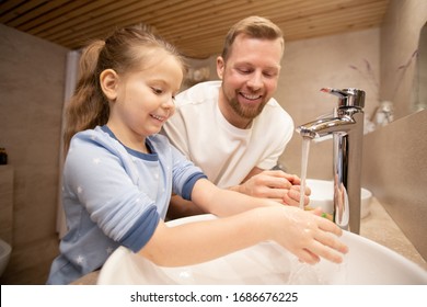 Happy young man looking at his cute little smiling daughter washing hands with soap over sink while both standing in bathroom - Powered by Shutterstock