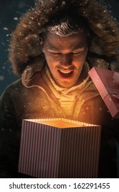 Happy Young Man Opening A Gift Box Outdoors At Night On Christmas Eve